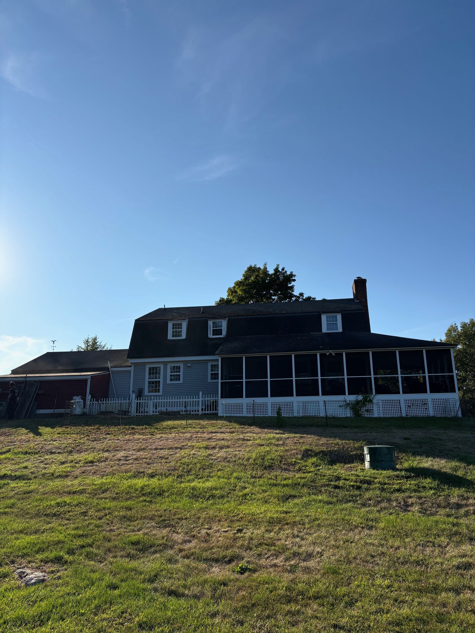Two-story house with weathered siding, screened porch, and dormers against a blue sky.