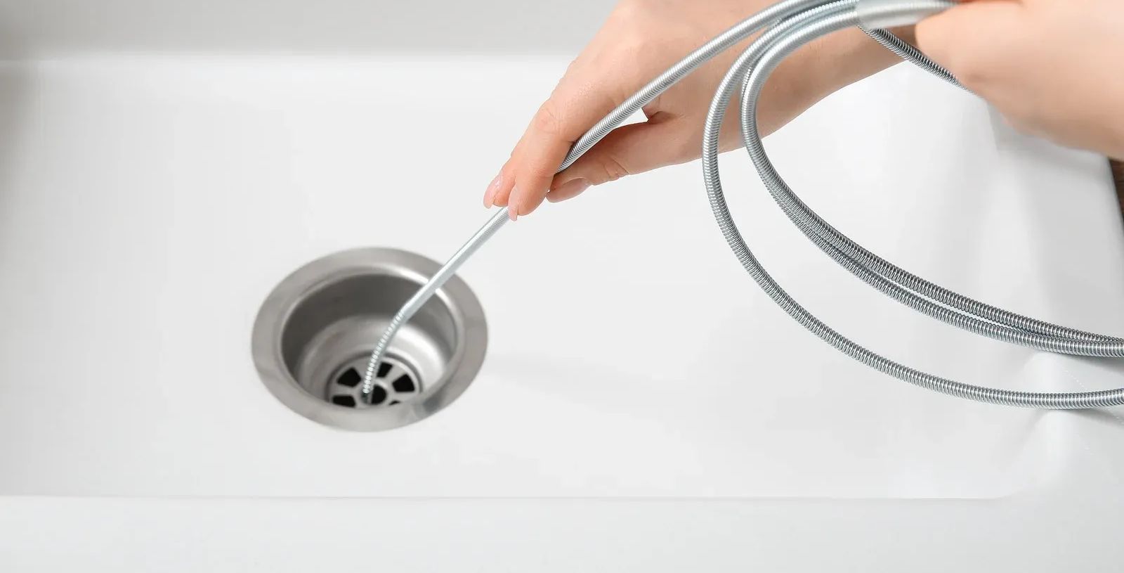 Hand using a silver sink snake to clear a white bathroom drain