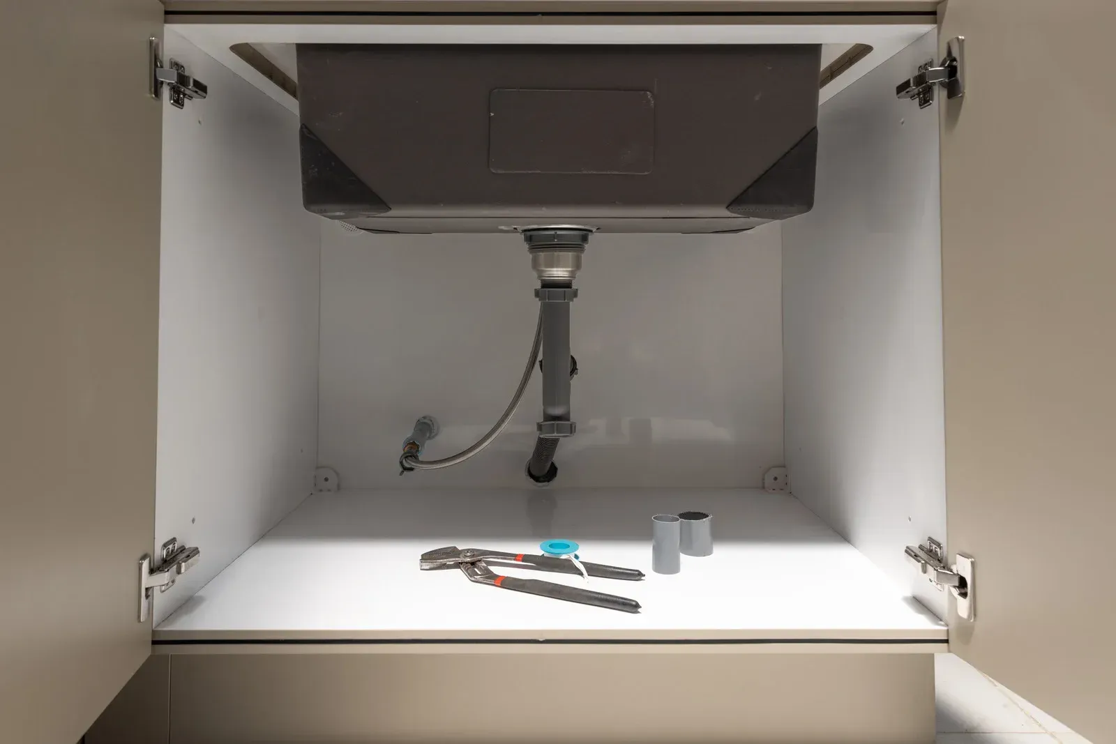 Sink cabinet interior with plumbing, tools, and a sink.