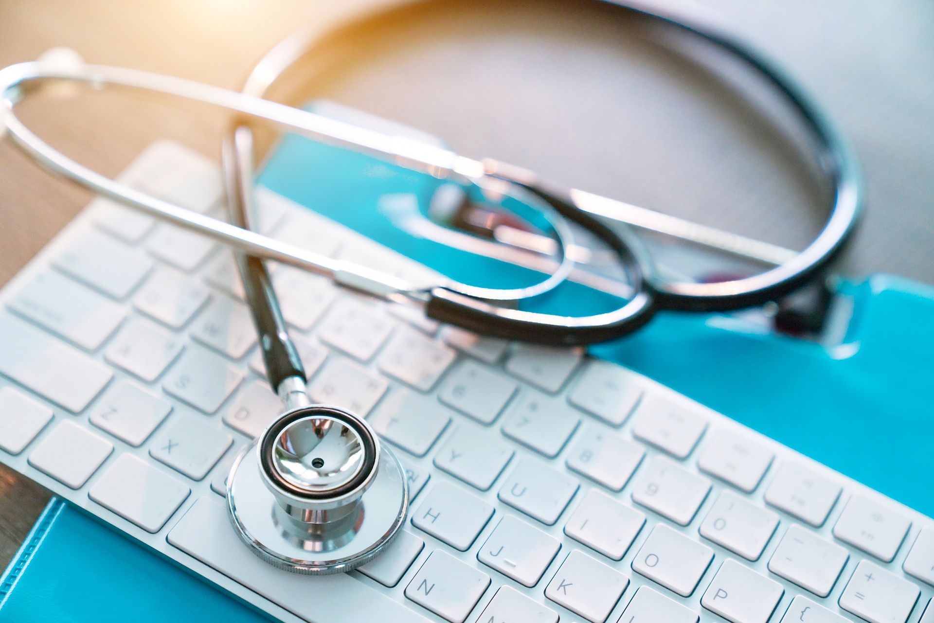 Stethoscope on a white keyboard and blue document holder, likely in a medical office setting.