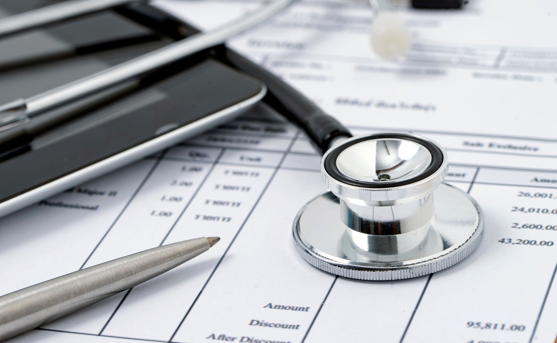 Stethoscope, tablet, and pen on top of medical bills and paperwork, indicating healthcare costs.