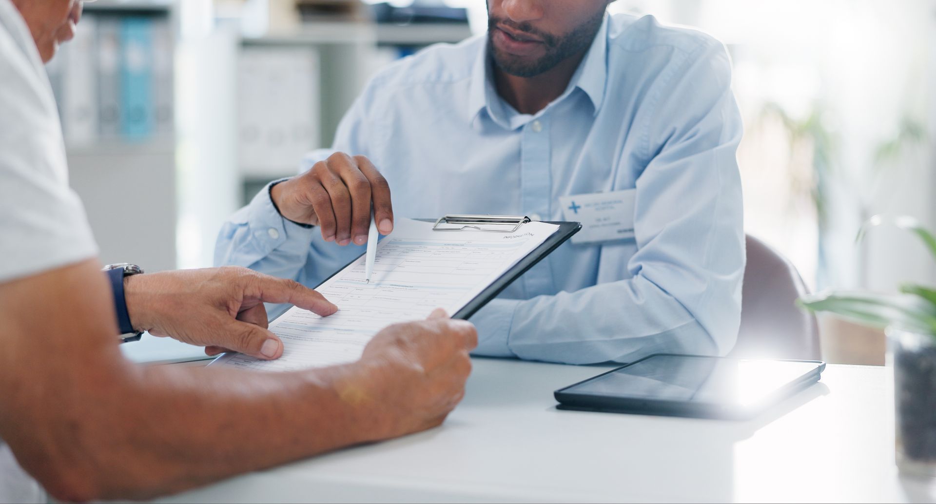 Two men reviewing paperwork at a desk; one points at the document.