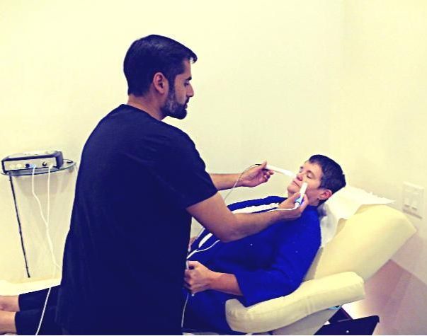 A man in a black shirt is talking to a boy in a blue robe laying in a chair.
