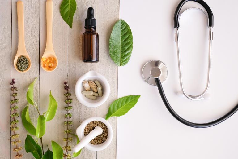 A stethoscope is sitting on a wooden table next to a bowl of herbs.
