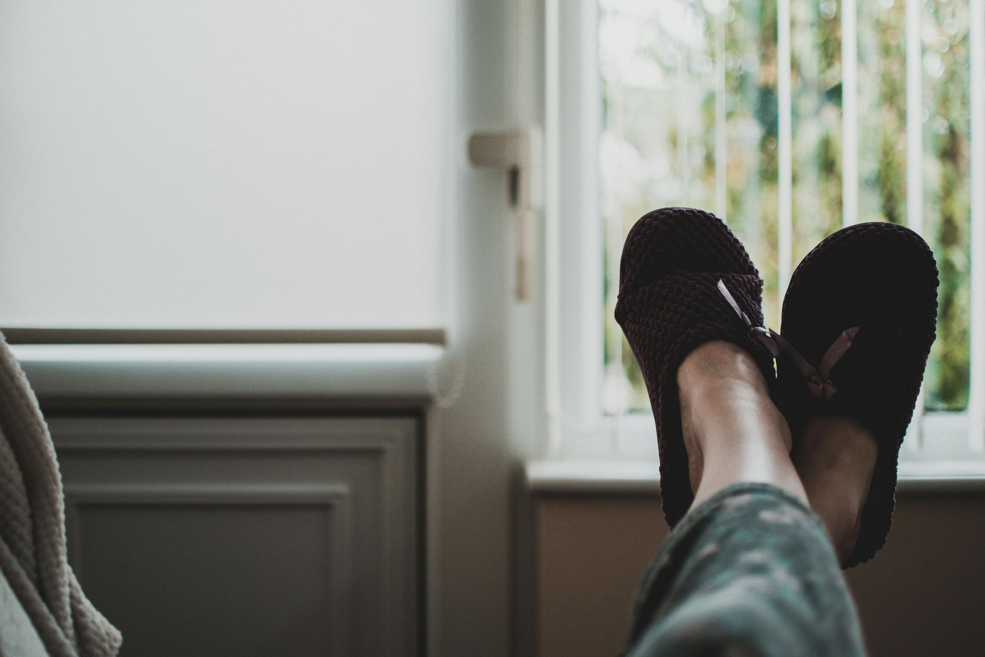 A person is laying on a couch with their feet up and wearing slippers.