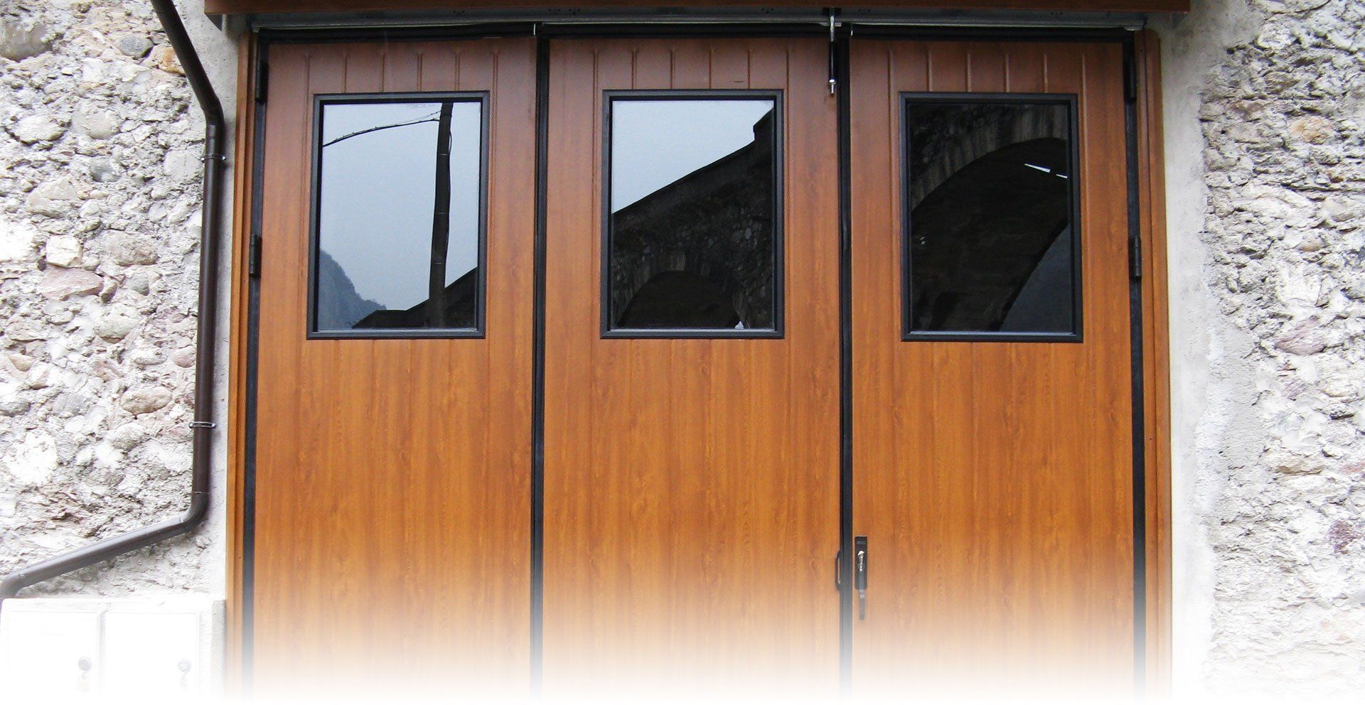 Una porta da garage in legno con tre finestre su un muro di pietra
