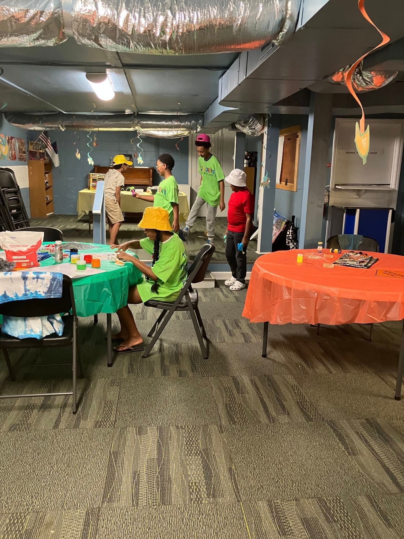 People in a room with activity tables, some wearing hats and bright green shirts, participating in a group event.