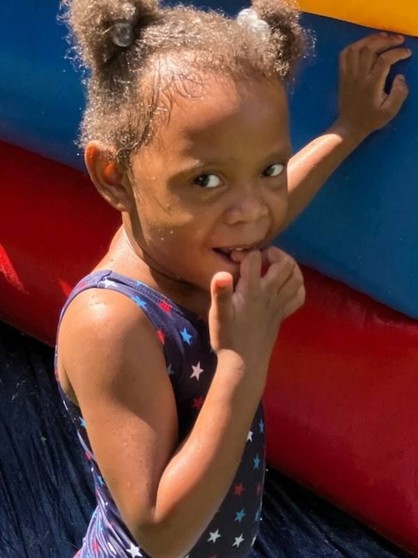 A child in a star-patterned swimsuit playfully touching their lip while standing against a red and blue inflatable surface.