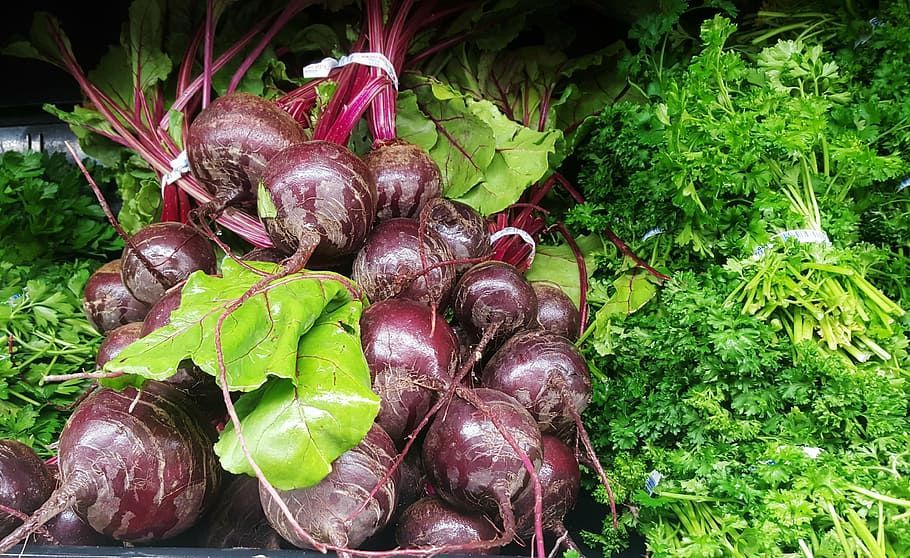 Fresh red beets with green leafy tops bunched together next to a large pile of fresh curly parsley.
