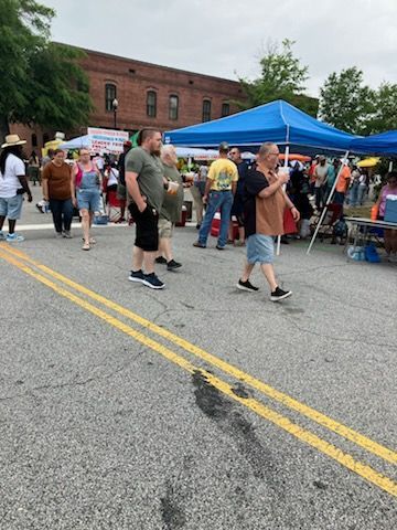 People walk past colorful vendor tents at an outdoor street fair on a cloudy day in front of a brick building.
