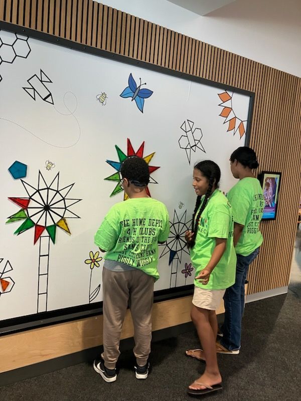 Three individuals in lime green shirts work together on a large geometric wall mural in a modern indoor space.