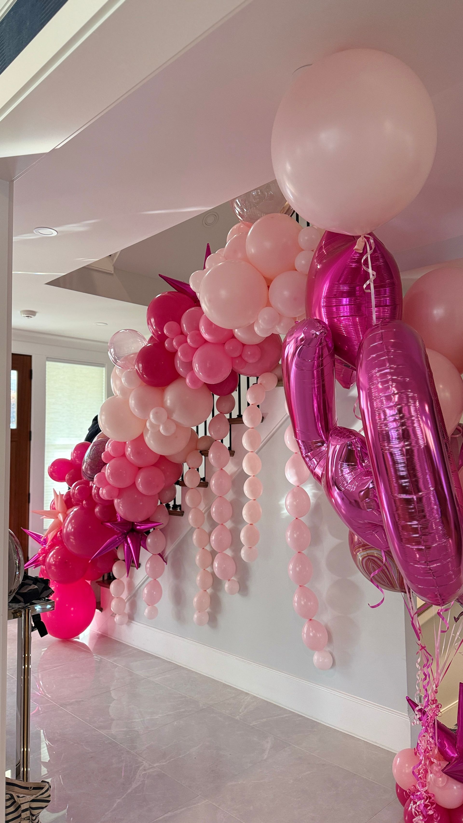 Pink and white organic balloon garland decorates a staircase. Balloons cascade down and cluster at the top.