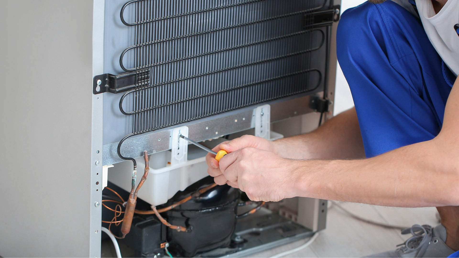 A man is fixing a refrigerator with a screwdriver.