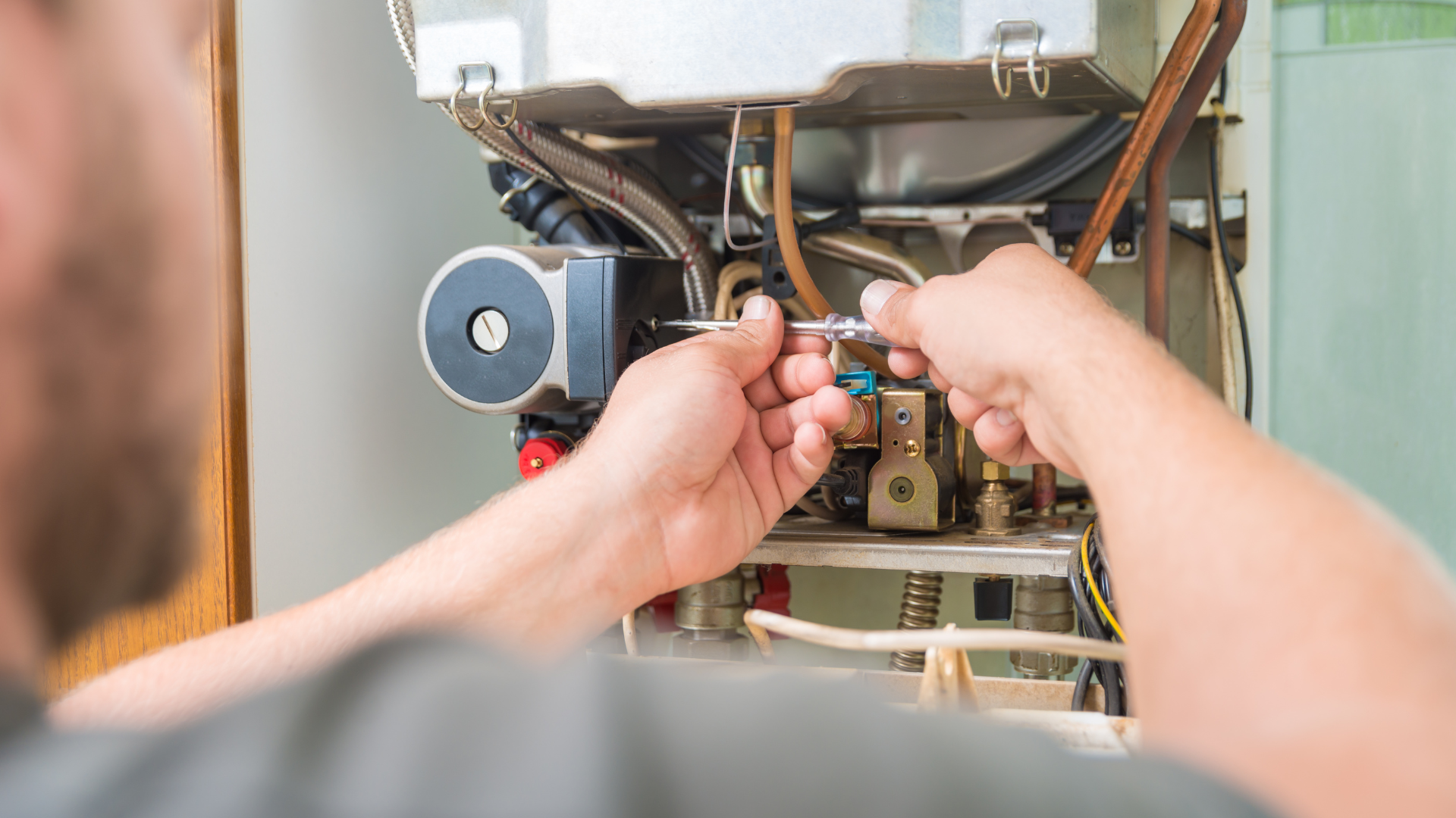 A man is fixing a boiler with a screwdriver.