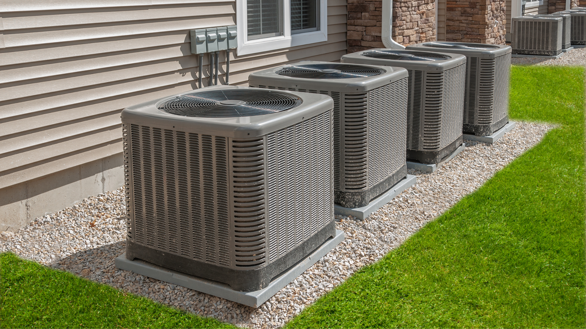 A row of air conditioners are sitting on the side of a house.