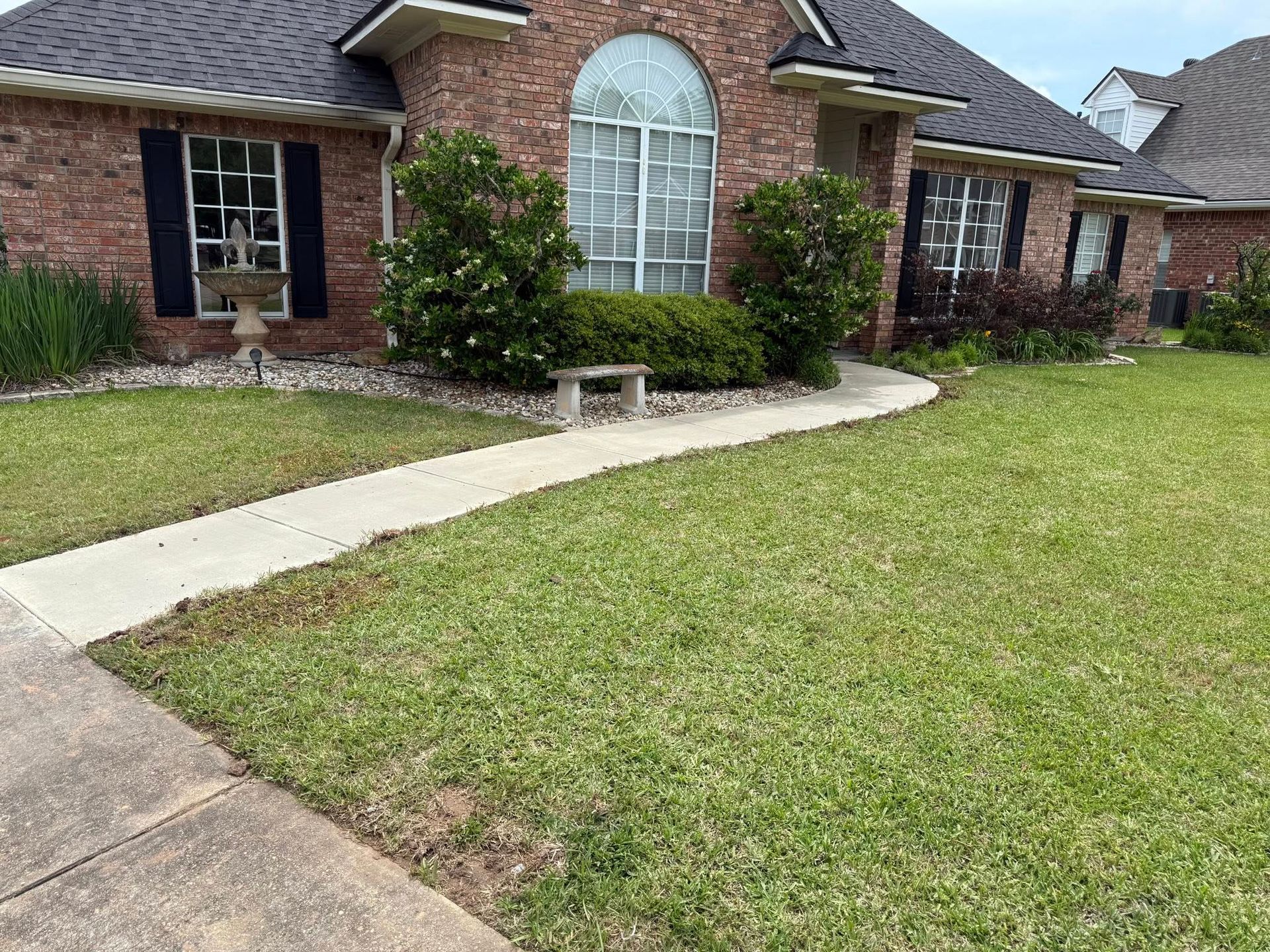 A brick house with a lush green lawn and a walkway leading to it.