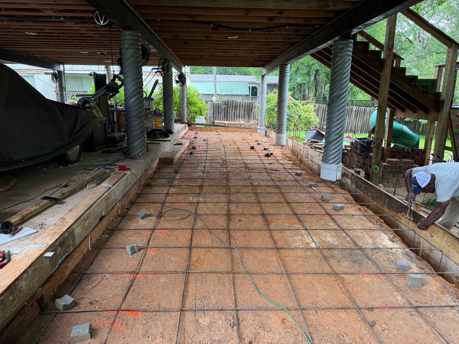 A man is working on a concrete driveway under a house.