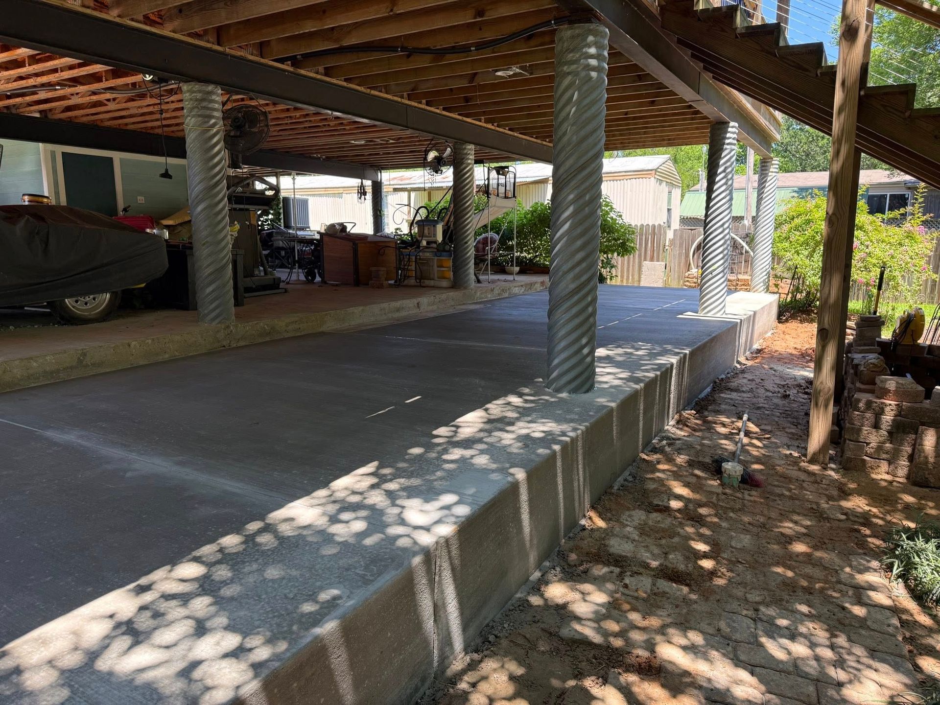 A car is parked under a covered porch in a driveway.