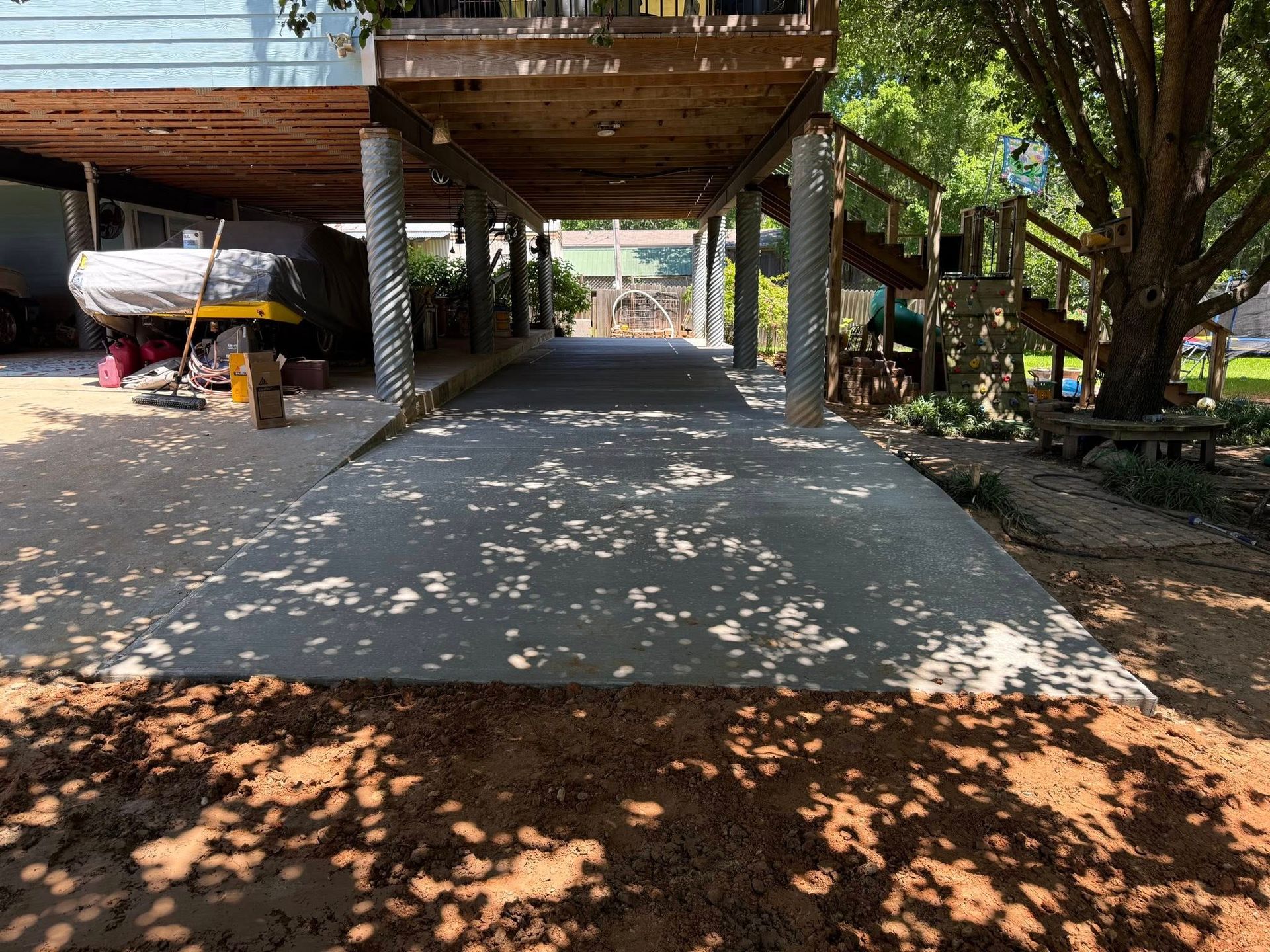 A concrete driveway leading to a house with a boat underneath it.