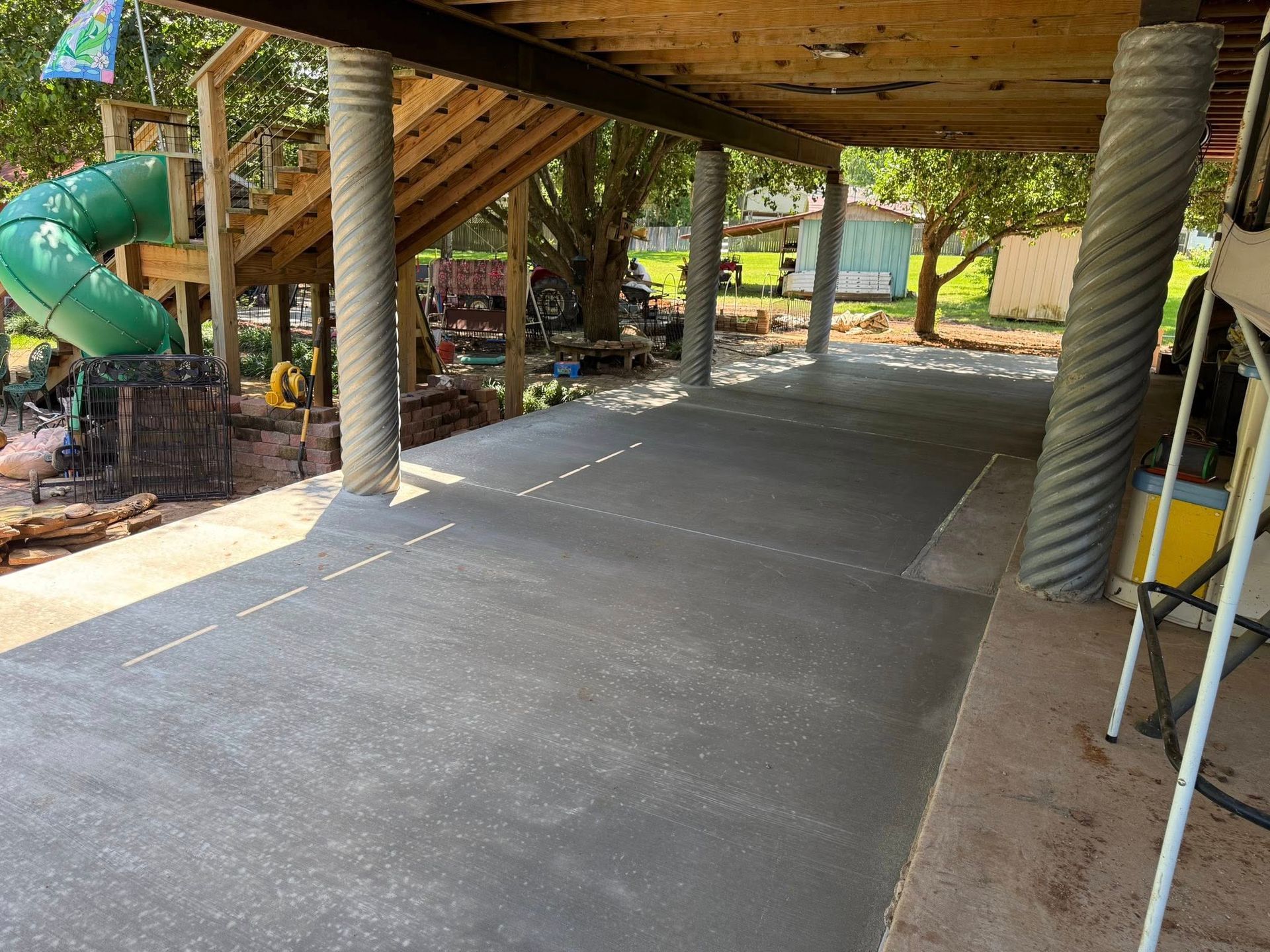 A concrete driveway under a wooden deck with a green slide in the background.