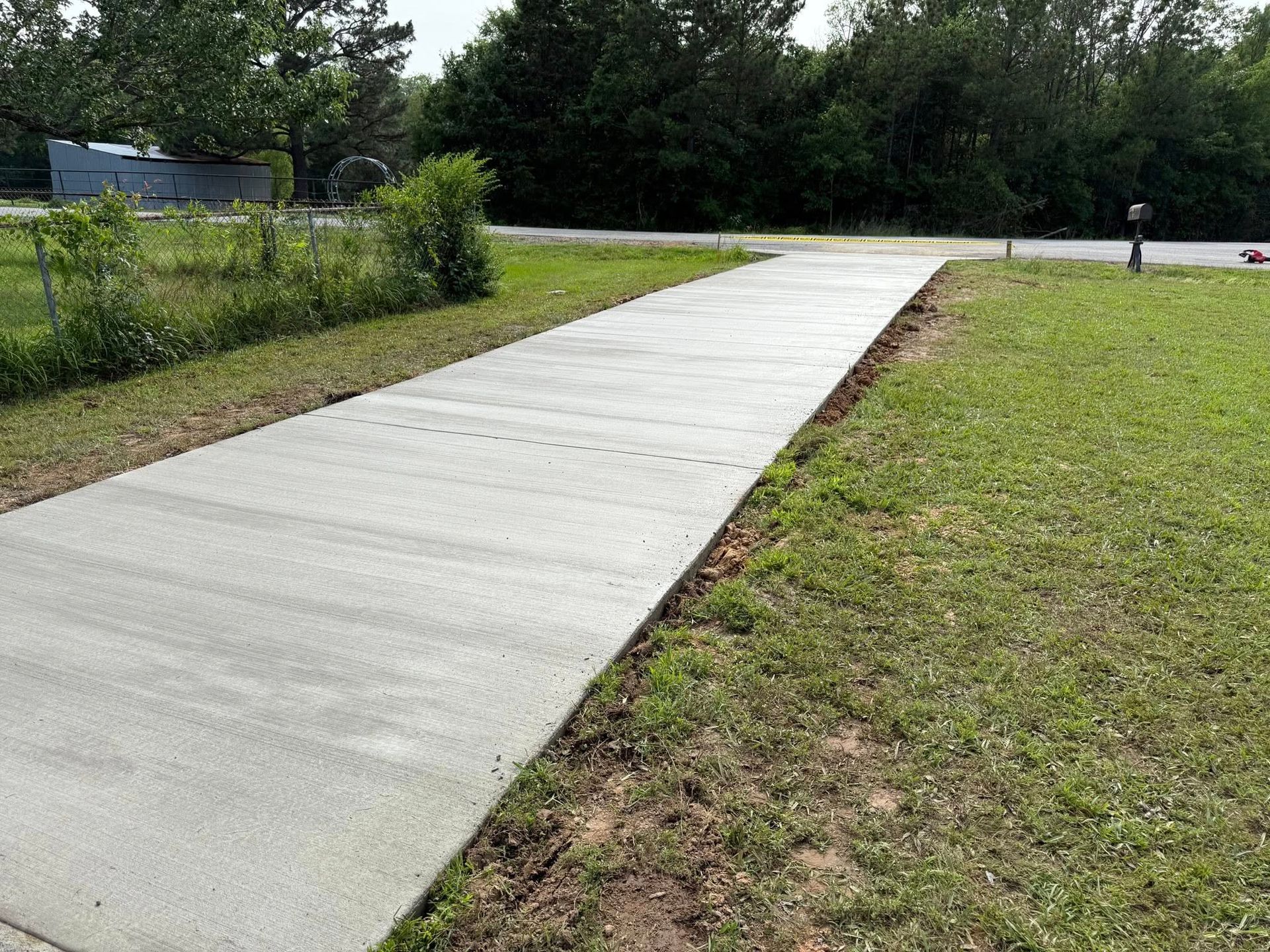 A concrete walkway going through a grassy field next to a road.