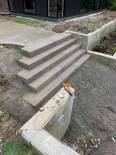 Concrete stairs lead to a modern building, situated next to a retaining wall and gravel construction site.