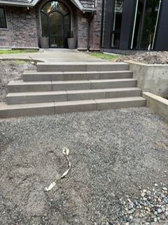 Concrete steps leading to a house entrance, with an unfinished gravel area in the foreground and retaining walls.