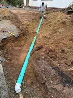 A worker in a trench installing green PVC drain pipes next to a building.