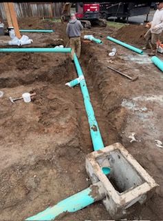 Construction workers installing green PVC drainage pipes in trenches at a job site with a catch basin.