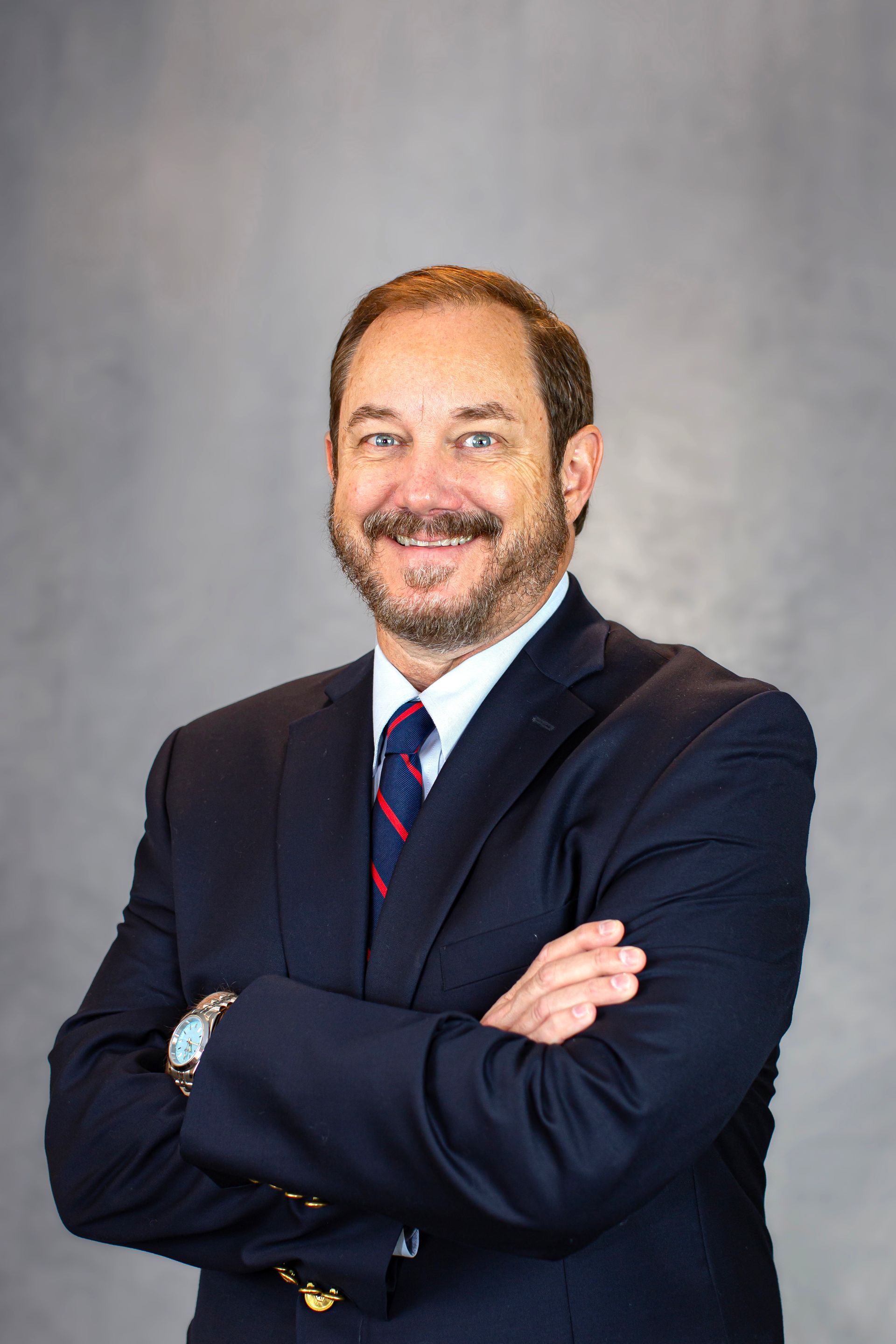 A man in a suit and tie is standing with his arms crossed.