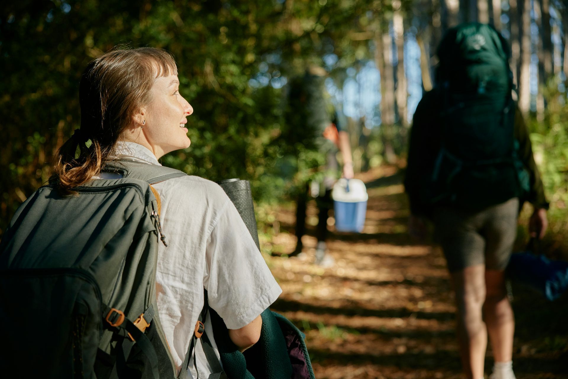 A woman with a backpack is walking down a path in the woods.