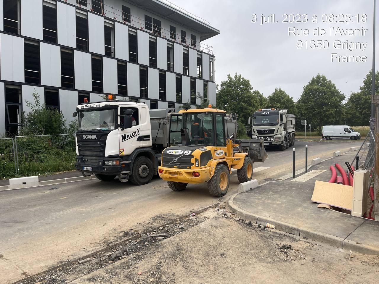 Un camion et un bulldozer sont garés sur le bord de la route devant un immeuble.