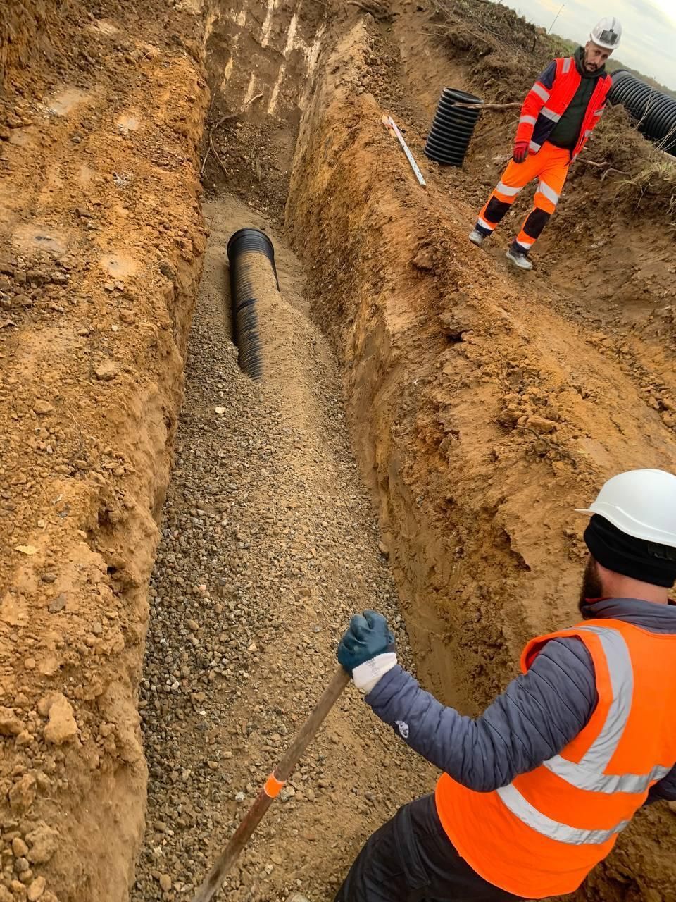 Un homme vêtu d'un gilet orange creuse une tranchée avec une pelle.