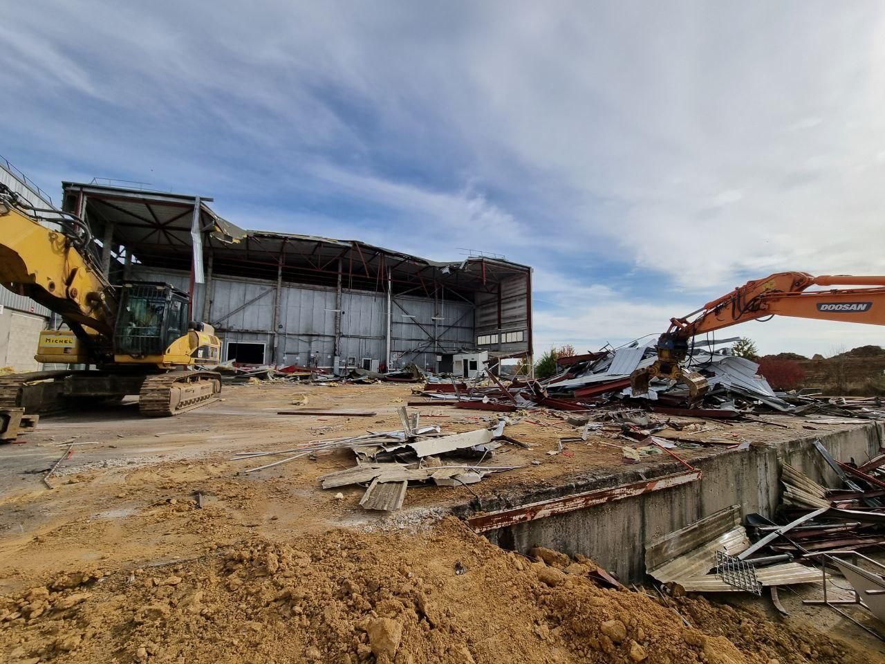 Un grand bâtiment est en train d'être démoli par une grande excavatrice.