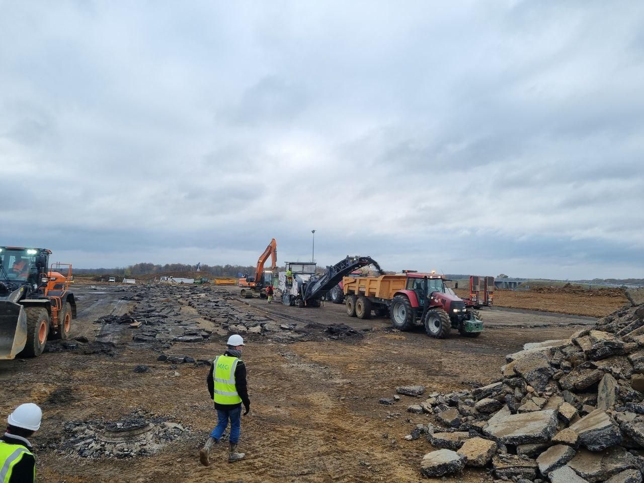 Un groupe d'ouvriers du bâtiment se tient dans un champ avec des tracteurs.