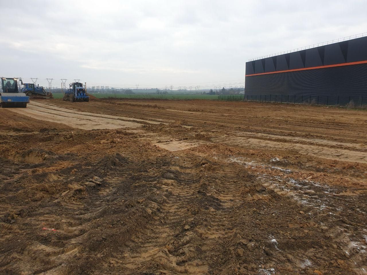 Un grand bâtiment est en construction au milieu d'un champ de terre.