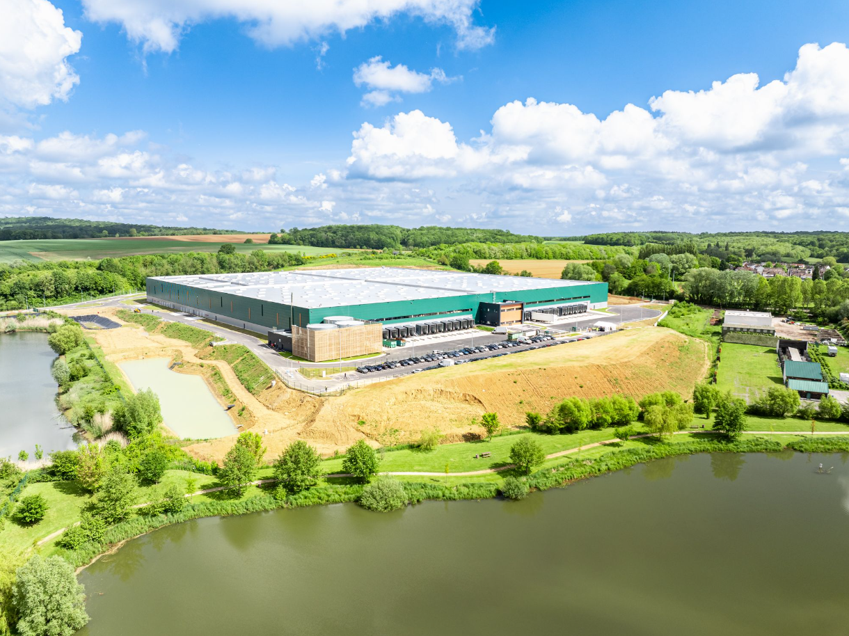 Une vue aérienne d'un grand bâtiment vert entouré d'arbres et d'un lac.