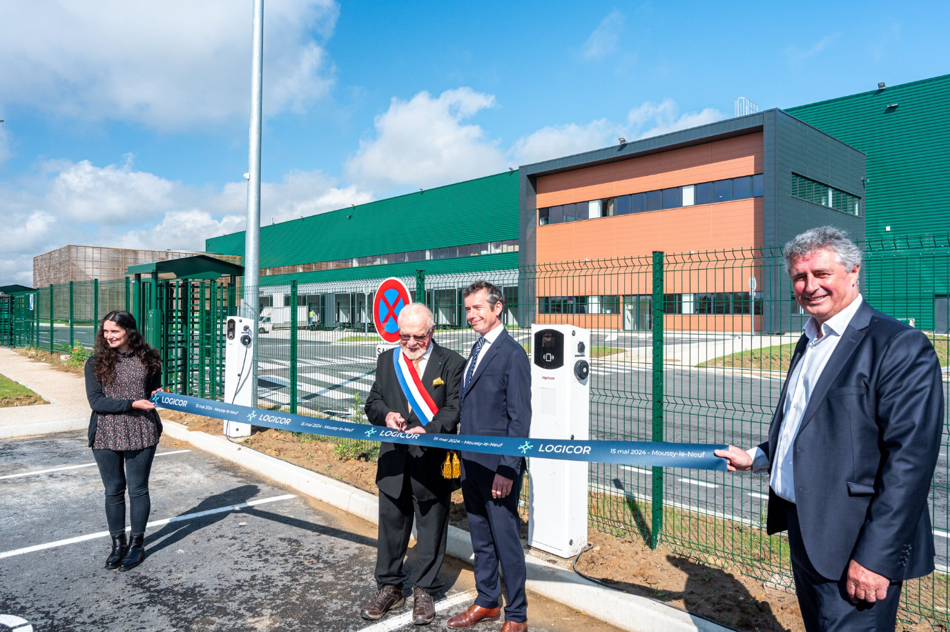 Un groupe de personnes se tient devant un bâtiment en train de couper un ruban.
