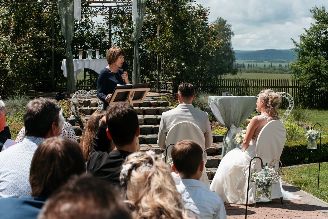 Eine Braut und ein Bräutigam sitzen bei einer Hochzeitszeremonie vor einer Menschenmenge.