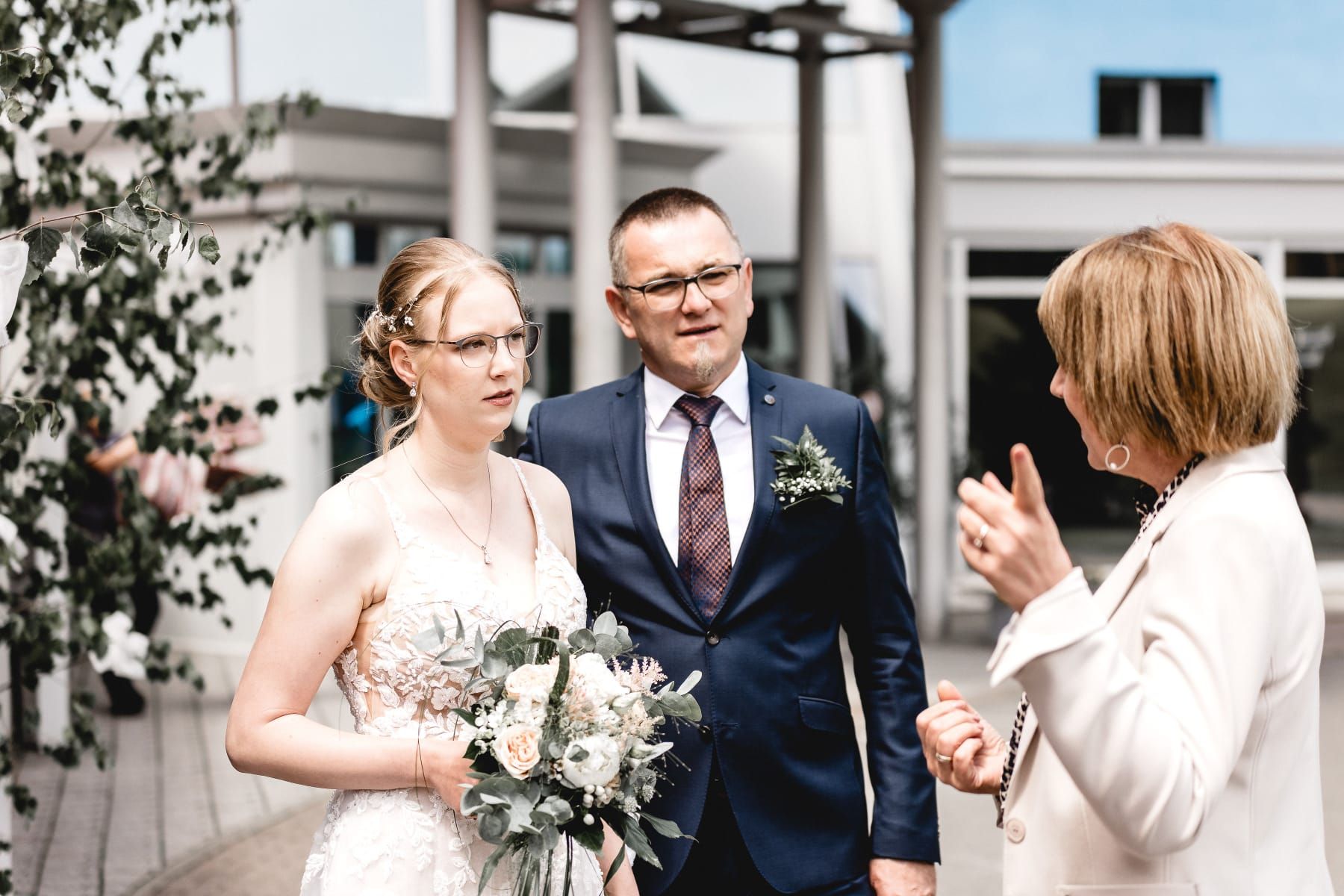 Eine Braut und ein Bräutigam stehen nebeneinander und unterhalten sich mit ihrer Hochzeitsrednerin.