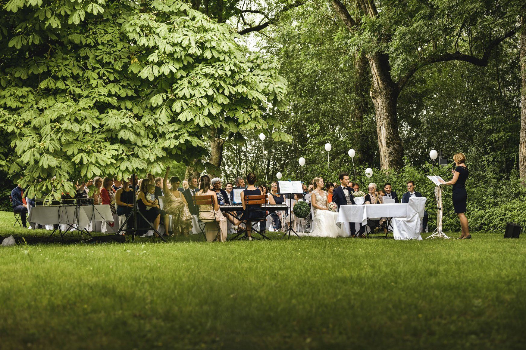 Eine Frau hält bei einer Hochzeitszeremonie in einem Park eine Rede.