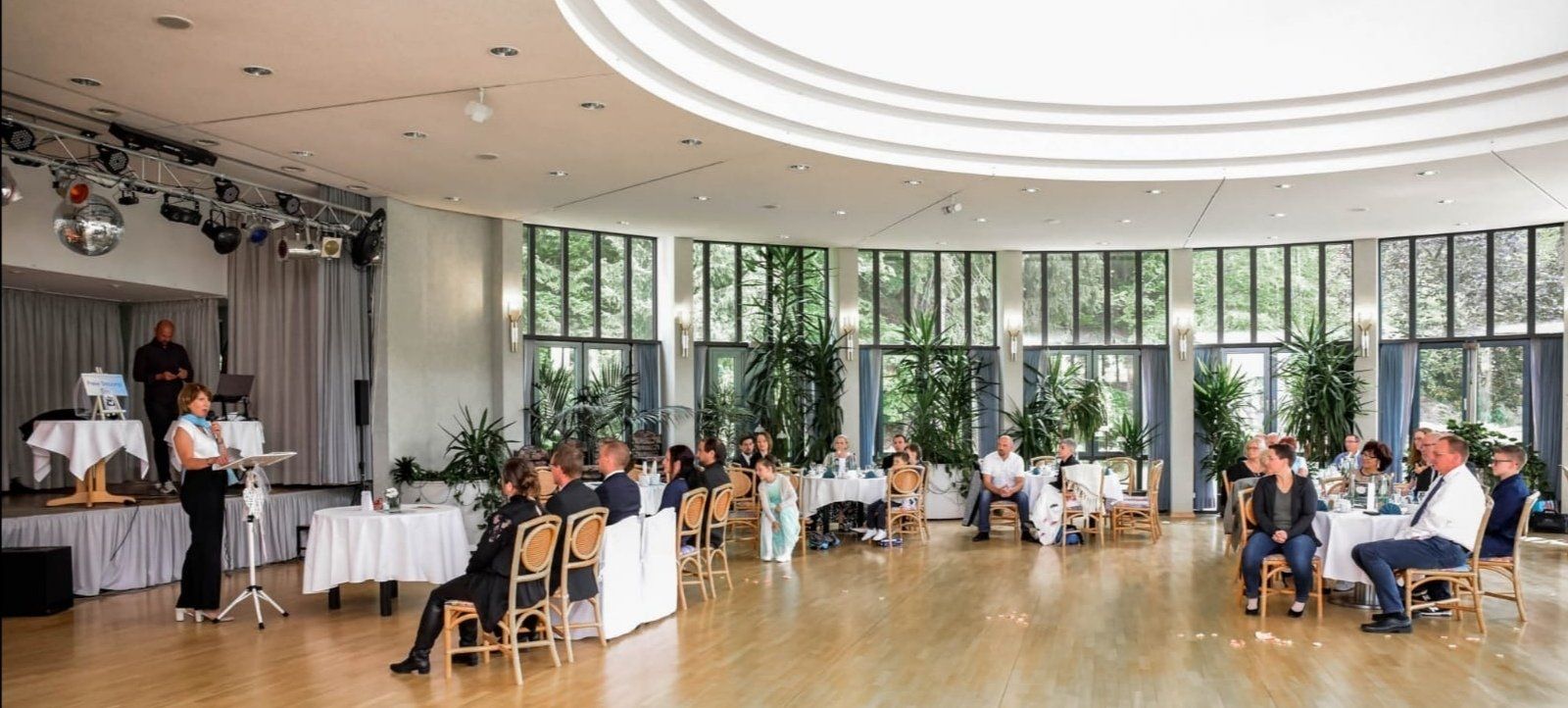 Eine Gruppe von Menschen sitzt während der Trauung in einem großen Raum an Tischen.