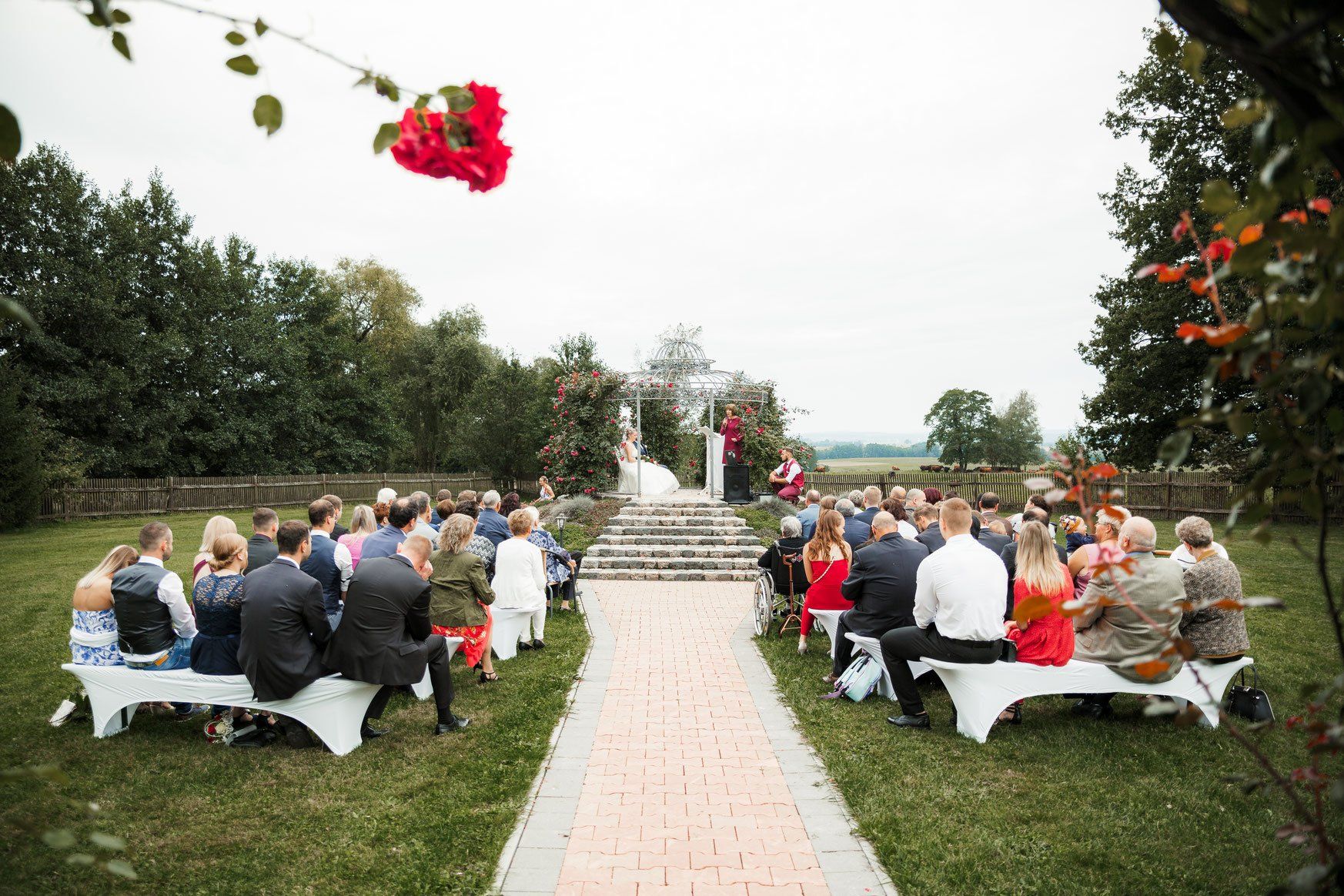 Eine Gruppe von Menschen sitzt bei einer Hochzeitszeremonie auf Bänken.