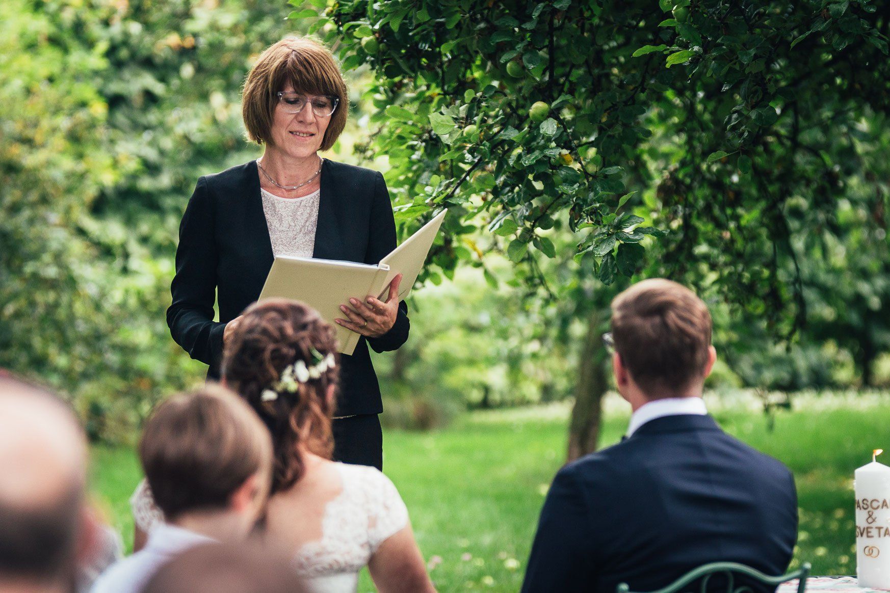 Bei einer Hochzeitszeremonie liest eine Frau einem Brautpaar aus einem Buch vor.