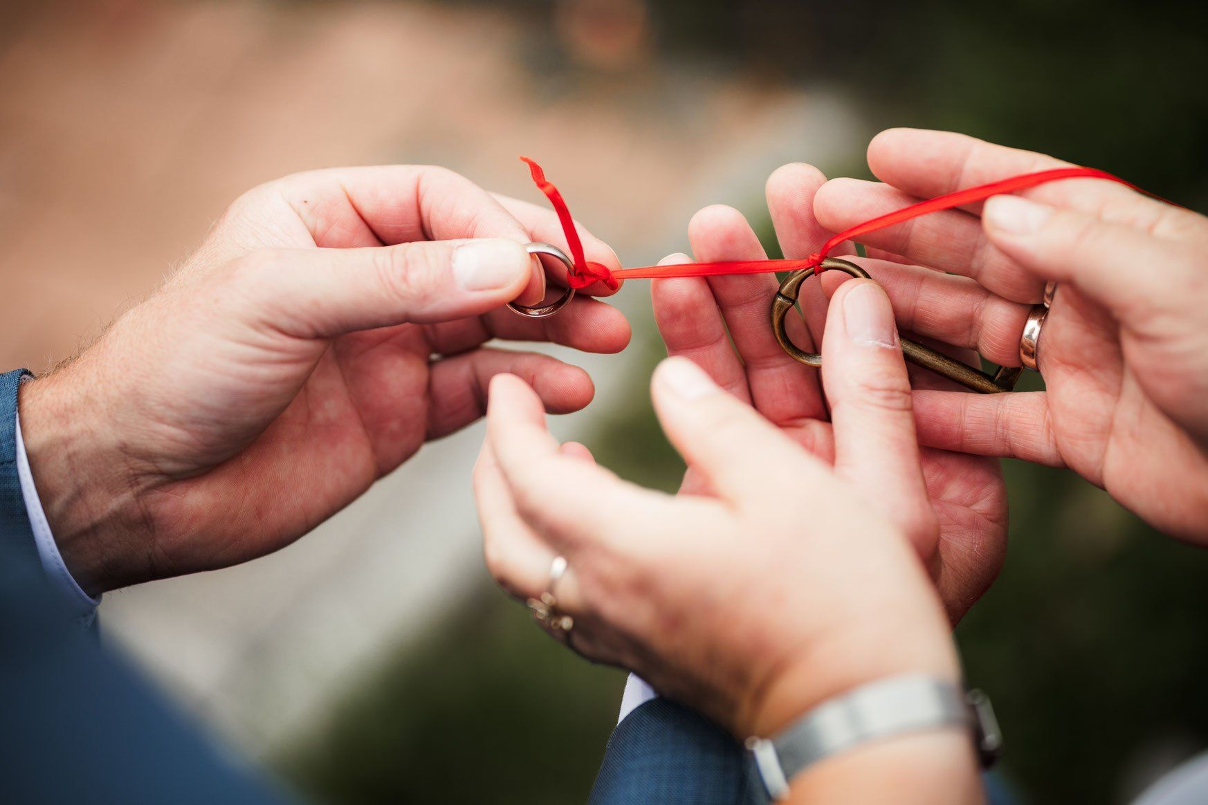 Ein Mann und eine Frau binden eine rote Schnur um einen Schlüssel und die Eheringe.