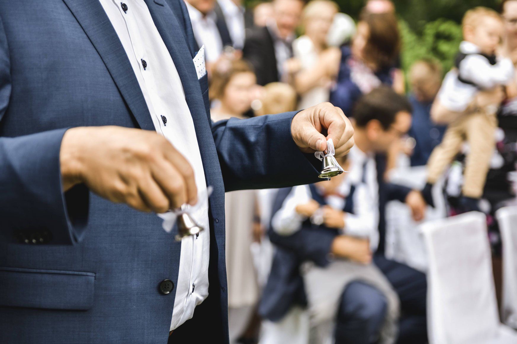 Bei einer Hochzeit hält ein Mann im Anzug eine Glocke in der Hand.