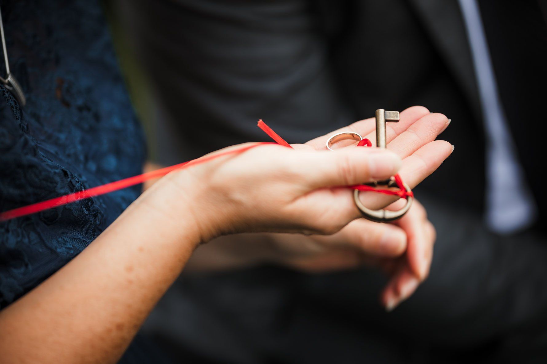 Eine Frau hält einen Schlüssel und die Eheringe, um den eine rote Schnur gebunden ist.