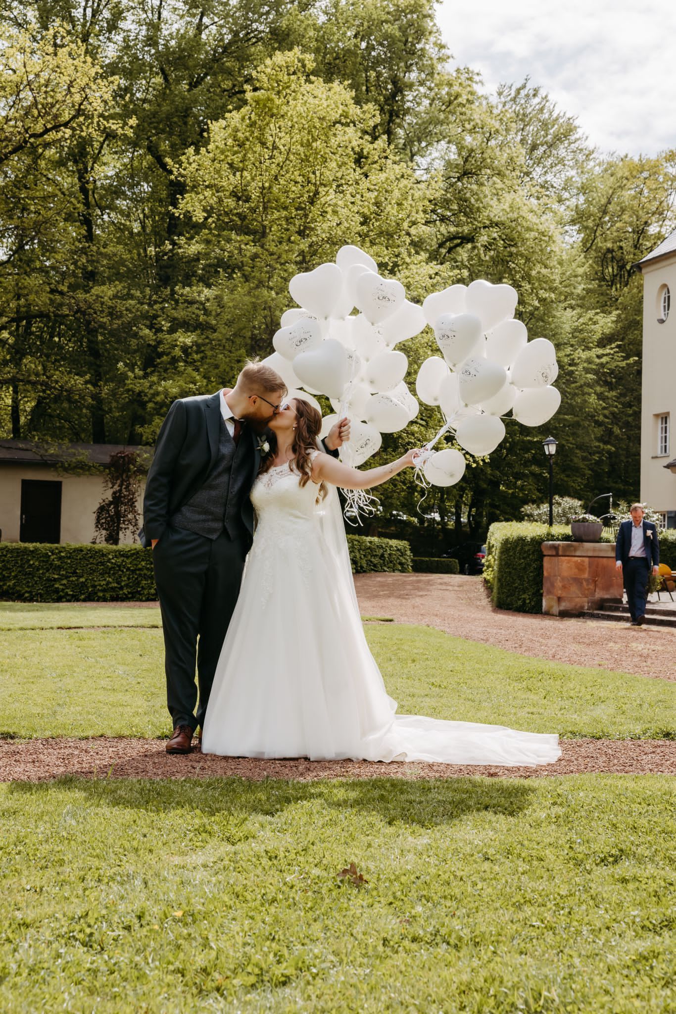 Eine Braut und ein Bräutigam stehen mit weißen Luftballons in der Hand auf einer Wiese.