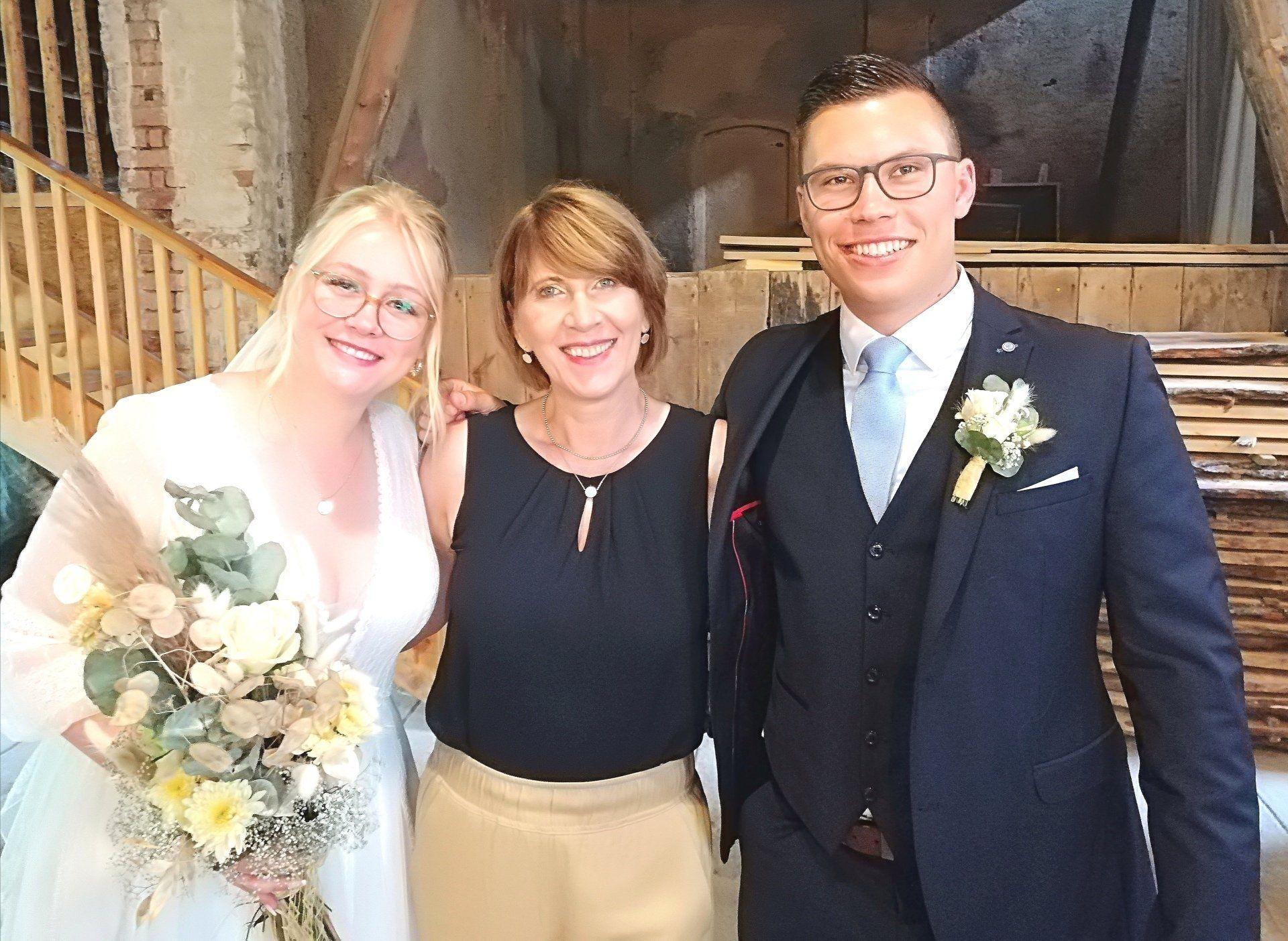 Ein Brautpaar posiert mit seiner freien Rednerin für ein Foto.