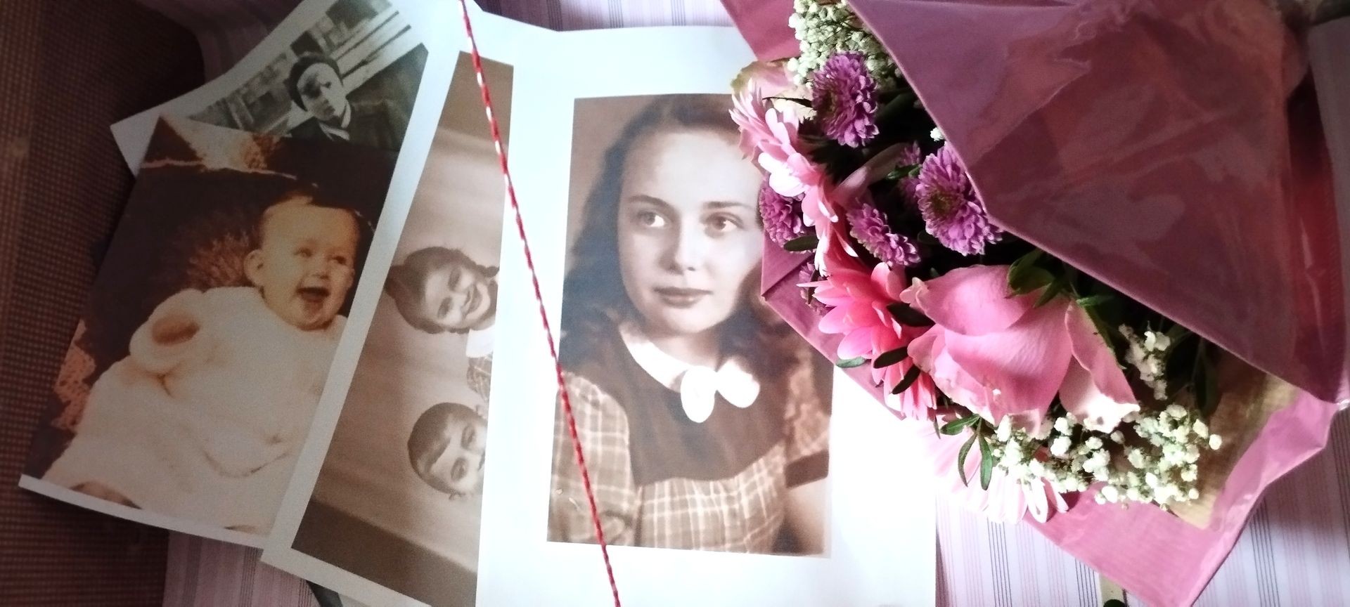 Ein Strauß rosa Blumen steht neben einem Stapel alter Fotos einer Frau.